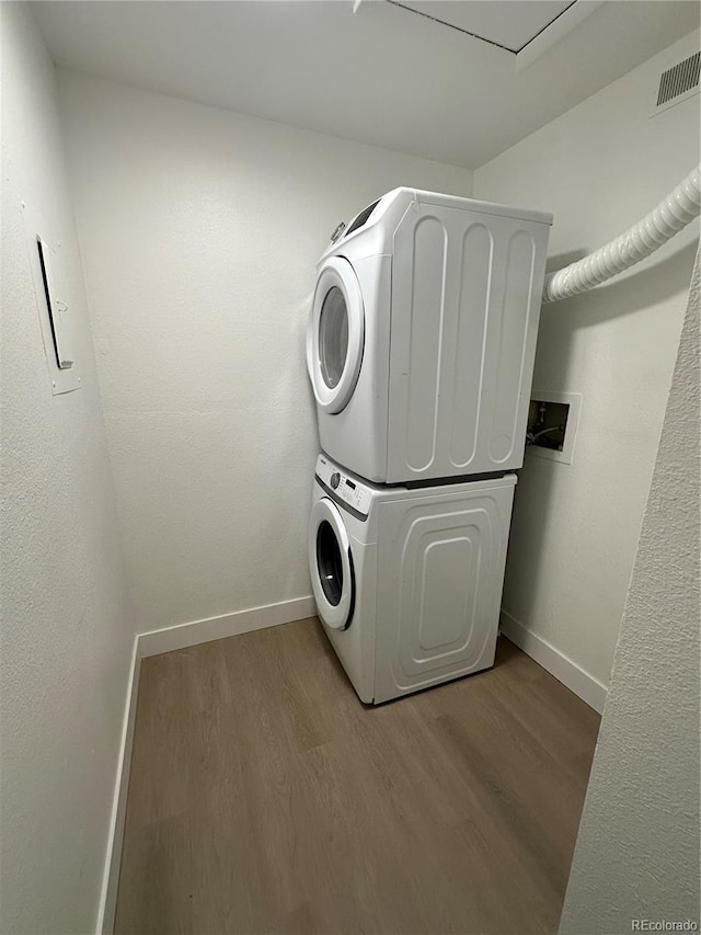 laundry room featuring visible vents, wood finished floors, stacked washer / dryer, baseboards, and laundry area