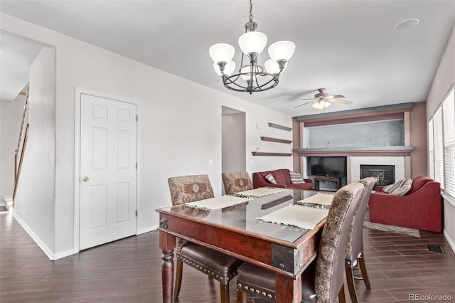 dining room featuring ceiling fan with notable chandelier, a tile fireplace, and dark hardwood / wood-style flooring