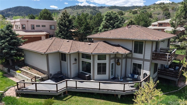 back of house with a deck with mountain view, a tile roof, a balcony, and a wooded view
