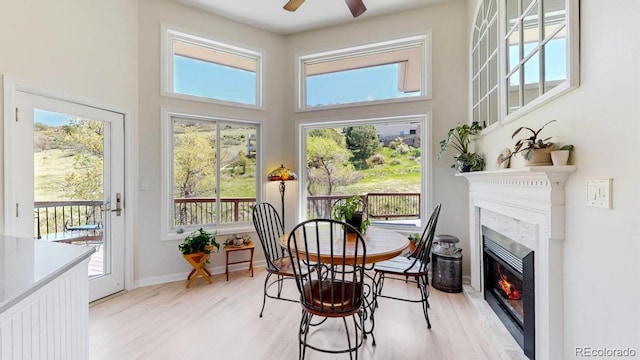 dining space featuring light wood finished floors, a ceiling fan, a glass covered fireplace, and a high ceiling