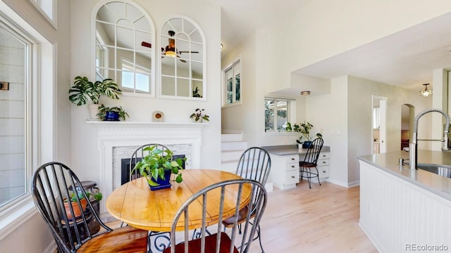 dining area featuring light wood-style floors, a fireplace, plenty of natural light, and arched walkways