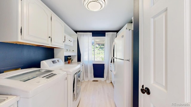 laundry area featuring washer and clothes dryer, light wood-style flooring, and cabinet space