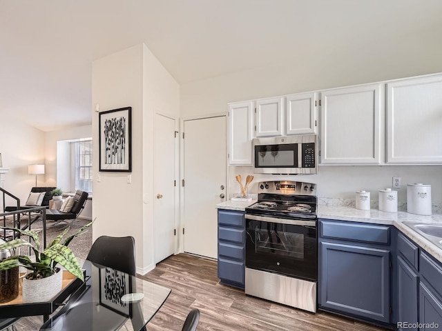 kitchen with blue cabinetry, appliances with stainless steel finishes, hardwood / wood-style flooring, and white cabinets