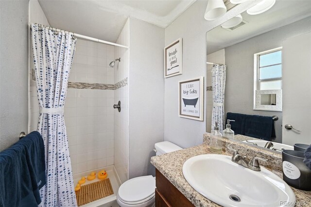 bathroom with vanity, toilet, tiled shower, and visible vents