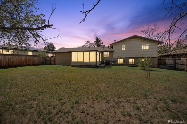 back of property with a fenced backyard, a sunroom, and a yard