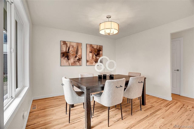 dining area with light wood-type flooring, visible vents, and baseboards