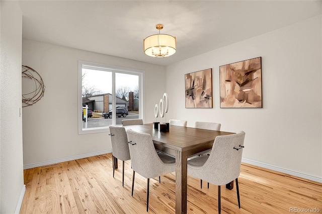 dining area featuring light wood-type flooring, baseboards, and a chandelier