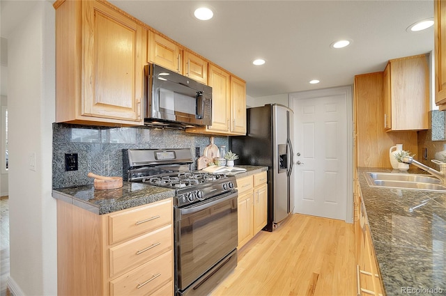 kitchen featuring light brown cabinetry, a sink, black appliances, light wood-style floors, and backsplash