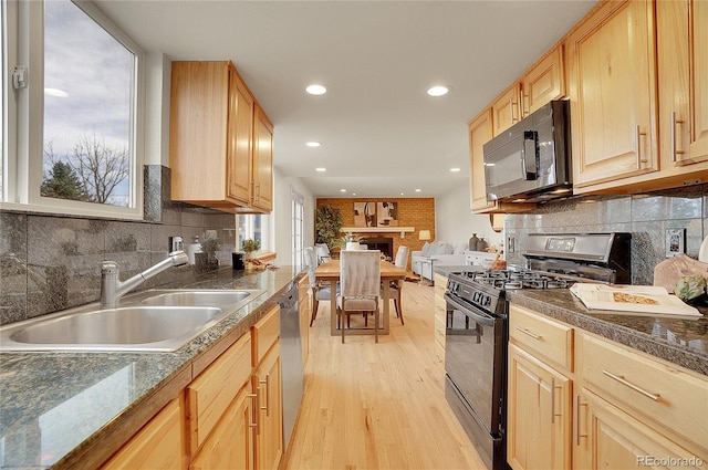 kitchen featuring light wood finished floors, light brown cabinetry, a sink, black appliances, and dark countertops