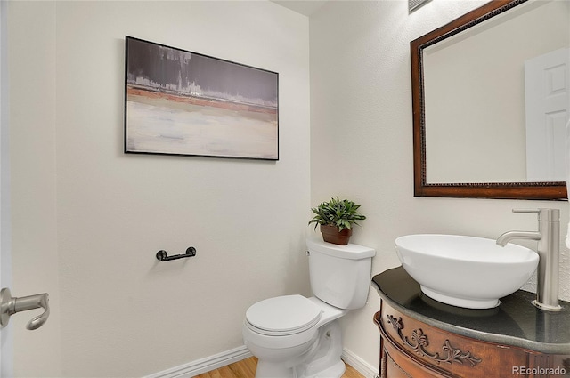 half bath featuring toilet, vanity, baseboards, and wood finished floors