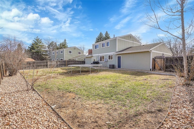 rear view of house featuring a trampoline, a lawn, cooling unit, and a fenced backyard