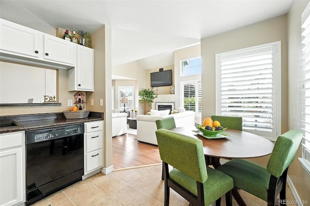 2567 Cutters Cir Unit 101, Castle Rock, CO 80108 - kitchen with dishwasher, a glass covered fireplace, dark countertops, white cabinetry, and vaulted ceiling