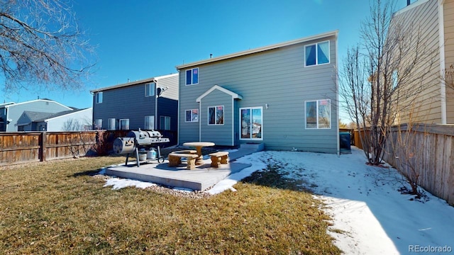 snow covered rear of property featuring a fenced backyard, a lawn, and a patio