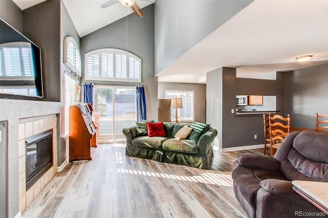 living room featuring high vaulted ceiling, wood finished floors, baseboards, ceiling fan, and a tile fireplace