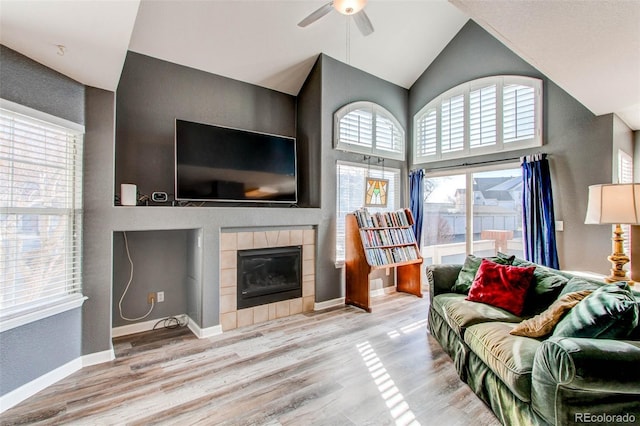 living room with high vaulted ceiling, wood finished floors, baseboards, ceiling fan, and a tile fireplace