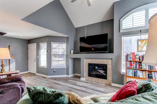 living room with vaulted ceiling, a tile fireplace, baseboards, and wood finished floors