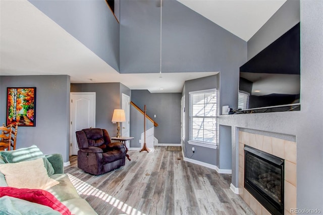 living area featuring a fireplace, high vaulted ceiling, baseboards, and wood finished floors