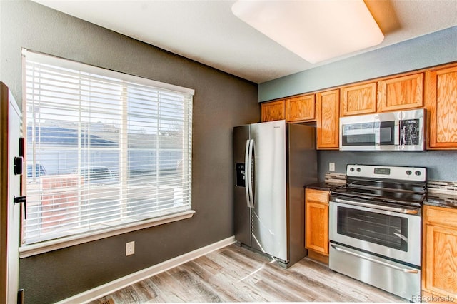 kitchen with baseboards, brown cabinets, appliances with stainless steel finishes, dark countertops, and light wood-type flooring