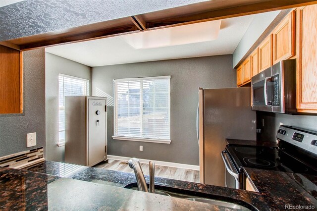 kitchen with a textured wall, stainless steel appliances, baseboards, and light wood finished floors