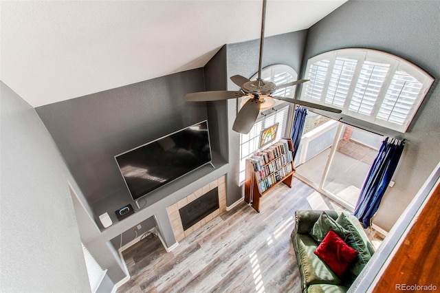 living area with a ceiling fan, lofted ceiling, wood finished floors, and a tiled fireplace