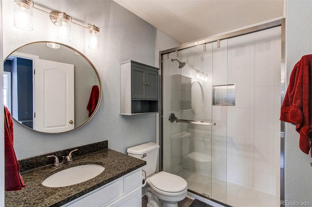 bathroom with vanity, toilet, a textured wall, and a stall shower