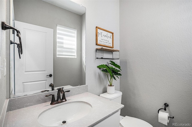 bathroom with a textured wall, toilet, and vanity
