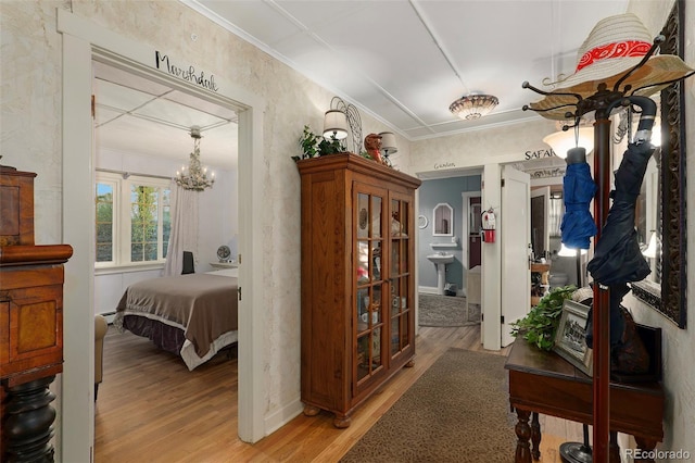 corridor with wood-type flooring, ornamental molding, and a chandelier