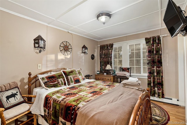 bedroom with baseboard heating, ornamental molding, and light hardwood / wood-style flooring