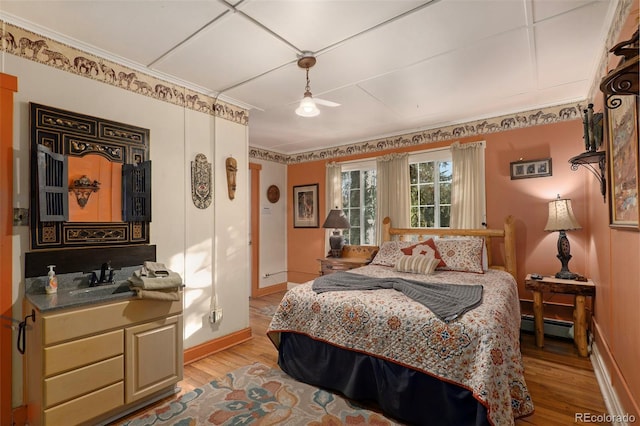 bedroom with a baseboard radiator, ceiling fan, light hardwood / wood-style flooring, ornamental molding, and sink