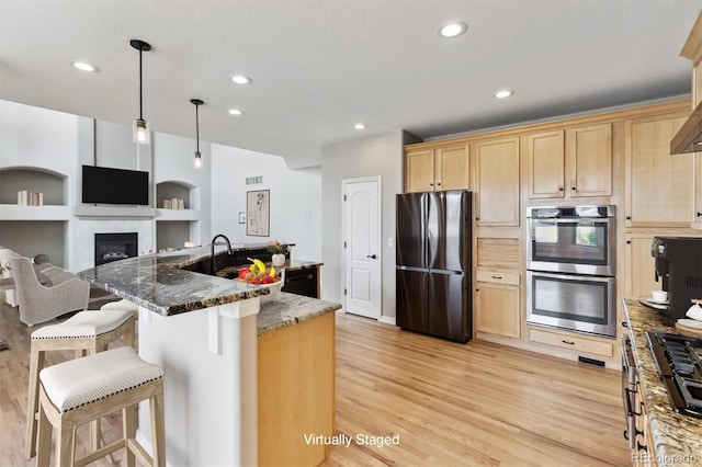 1328 Double Eagle Ct, Castle Rock, CO 80104 - kitchen featuring appliances with stainless steel finishes, light brown cabinetry, light wood-style flooring, a fireplace, and recessed lighting