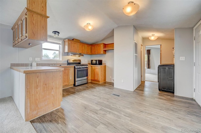 kitchen with a sink, under cabinet range hood, gas stove, light wood-style flooring, and light countertops