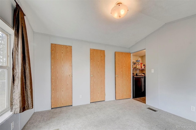 unfurnished bedroom with washer / dryer, carpet, multiple closets, visible vents, and vaulted ceiling