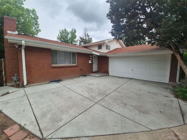 387 Tucson St, Aurora, CO 80011 - view of front of house featuring brick siding, a chimney, an attached garage, and driveway