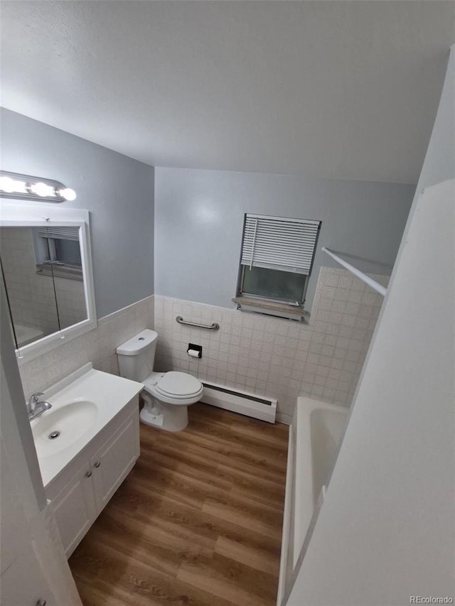 387 Tucson St, Aurora, CO 80011 - bathroom with tile walls, a baseboard radiator, toilet, wood finished floors, and a tub to relax in