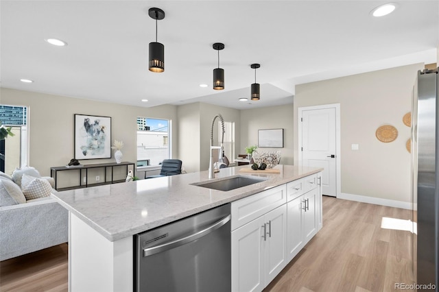 kitchen with white cabinetry, stainless steel appliances, decorative light fixtures, and an island with sink