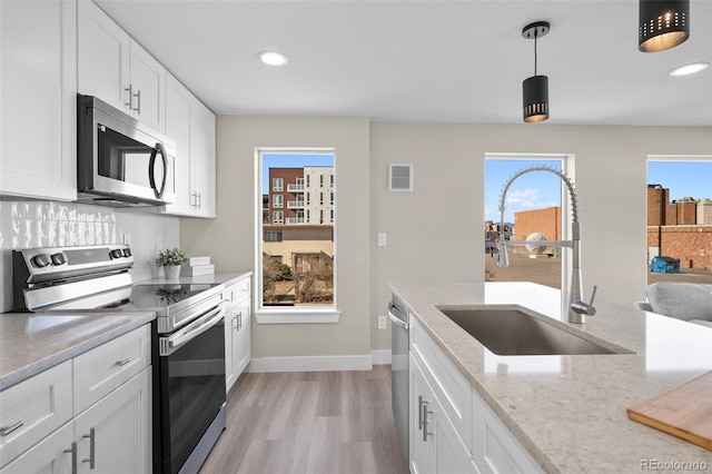 kitchen with sink, appliances with stainless steel finishes, white cabinetry, light stone counters, and decorative light fixtures