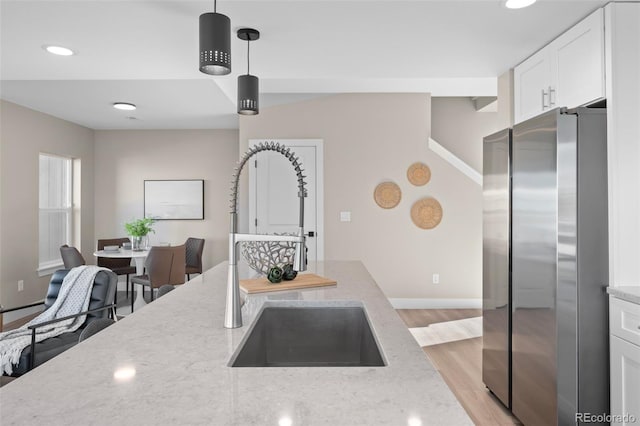 kitchen with a sink, white cabinets, freestanding refrigerator, and light stone countertops