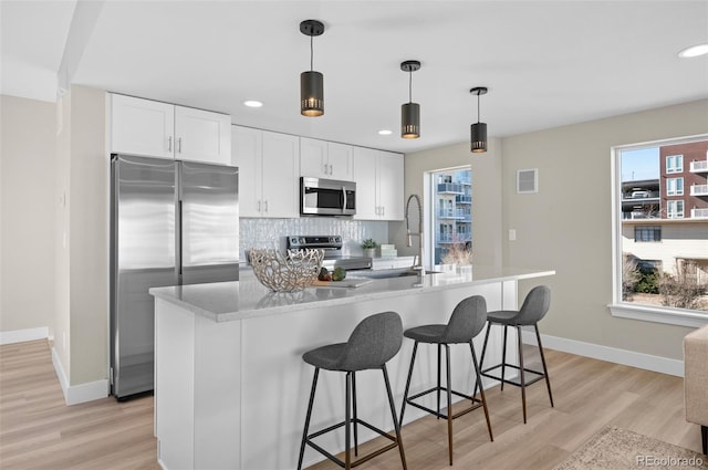 kitchen featuring white cabinetry, appliances with stainless steel finishes, an island with sink, and tasteful backsplash