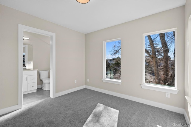 unfurnished bedroom with carpet floors, baseboards, ensuite bathroom, and multiple windows