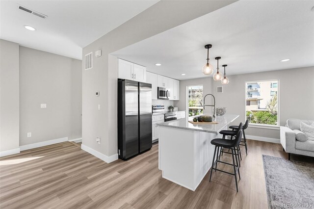 kitchen with visible vents, a sink, a breakfast bar, stainless steel appliances, and white cabinetry