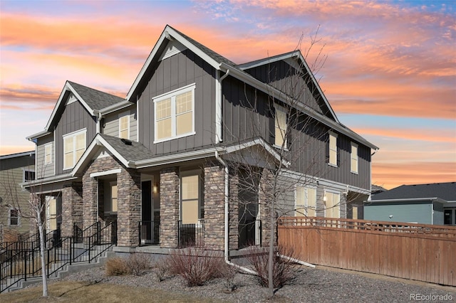 view of front facade featuring stone siding, fence, board and batten siding, and roof with shingles