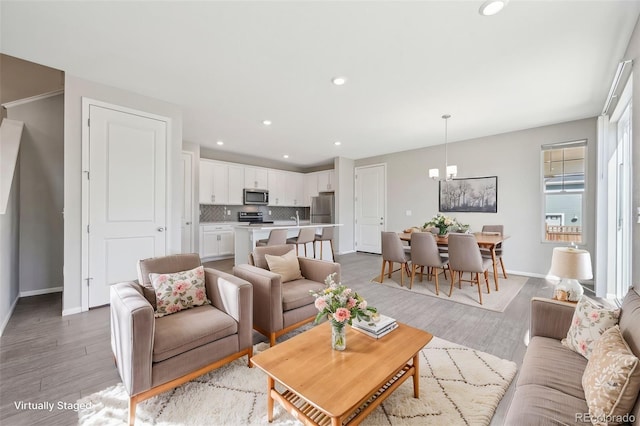 living room featuring baseboards, recessed lighting, an inviting chandelier, and light wood-style floors