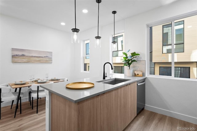 kitchen featuring dishwasher, sink, light wood-type flooring, decorative light fixtures, and kitchen peninsula