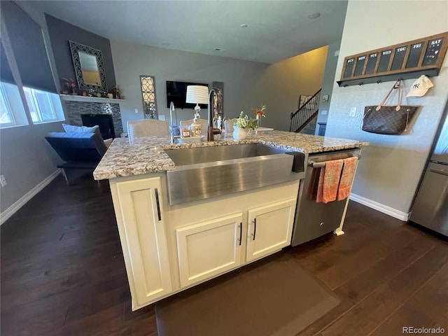 kitchen with a stone fireplace, dark wood-type flooring, a center island with sink, sink, and white cabinets