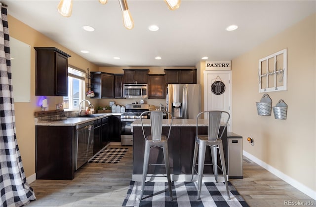 kitchen with sink, a center island, a breakfast bar, appliances with stainless steel finishes, and light wood-type flooring