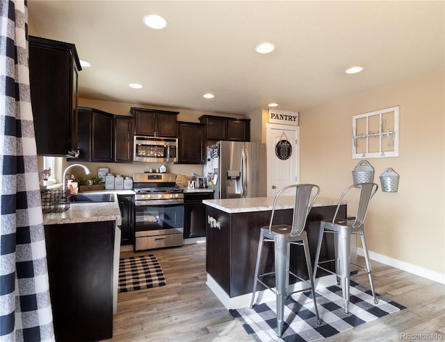 kitchen featuring a center island, sink, light stone countertops, light hardwood / wood-style floors, and stainless steel appliances