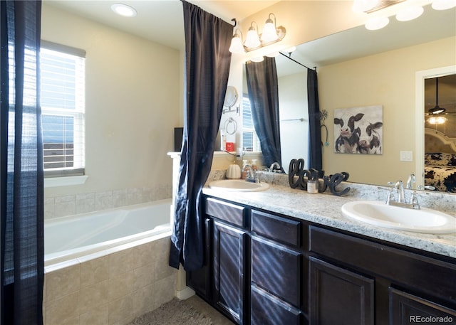 bathroom featuring a relaxing tiled tub, vanity, ceiling fan, and a wealth of natural light