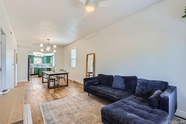living room featuring baseboards, ceiling fan with notable chandelier, and light wood-style flooring