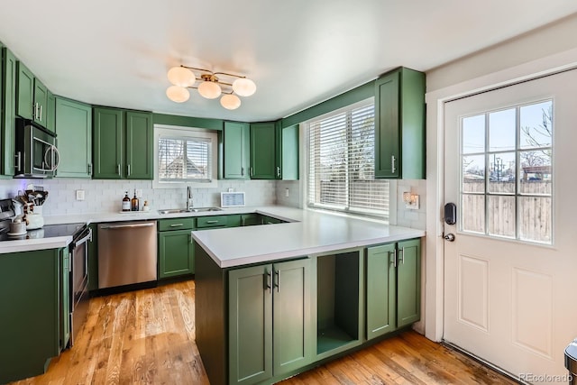 kitchen with stainless steel appliances, a peninsula, a sink, and green cabinets