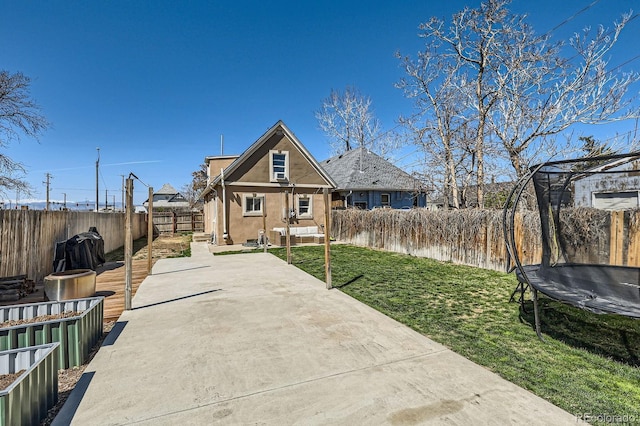 back of house featuring a trampoline, a patio area, a fenced backyard, a yard, and stucco siding